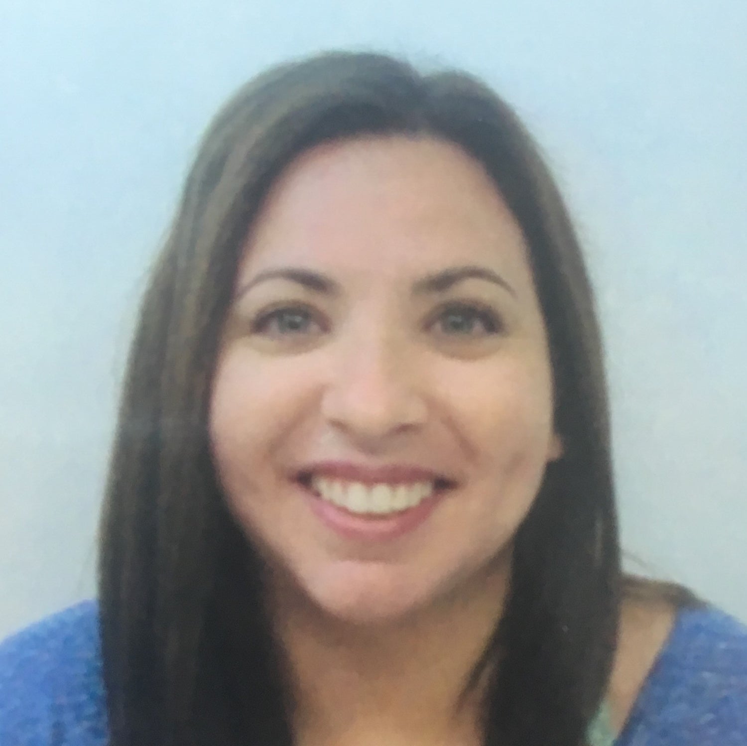 Smiling woman with straight brown hair wearing a blue top, posed against a plain light background, conveying a friendly and approachable professional presence.