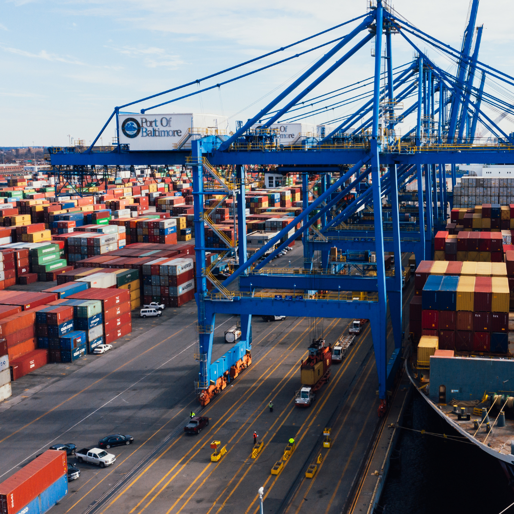 A busy shipping port featuring large blue cranes unloading colorful stacked freight containers from cargo vessels, illustrating global trade activity and logistics operations.