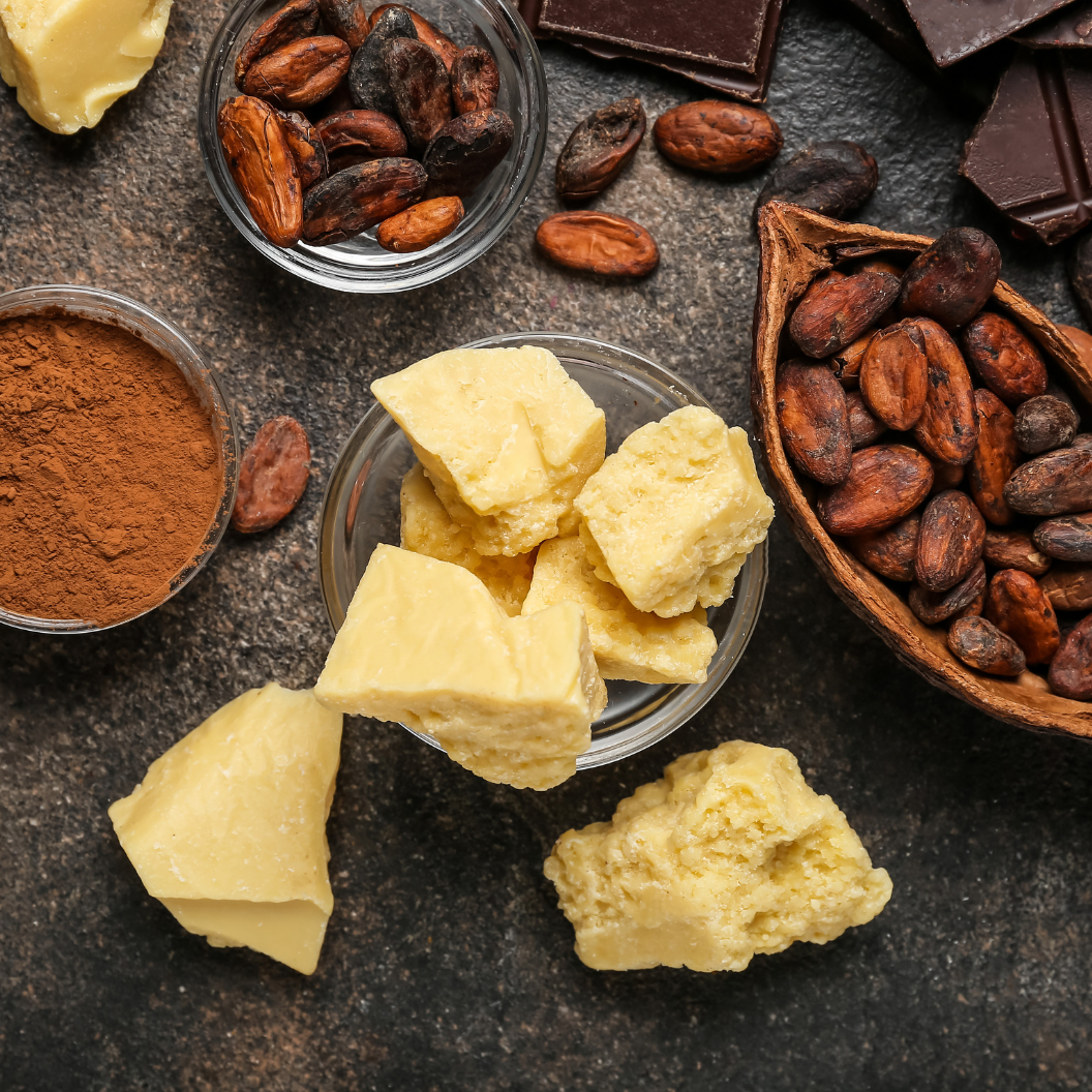 Chunks of creamy cocoa butter surrounded by roasted cocoa beans, cocoa powder, and dark chocolate pieces on a dark surface, illustrating expert insights and exclusive market analysis for commodity trends.