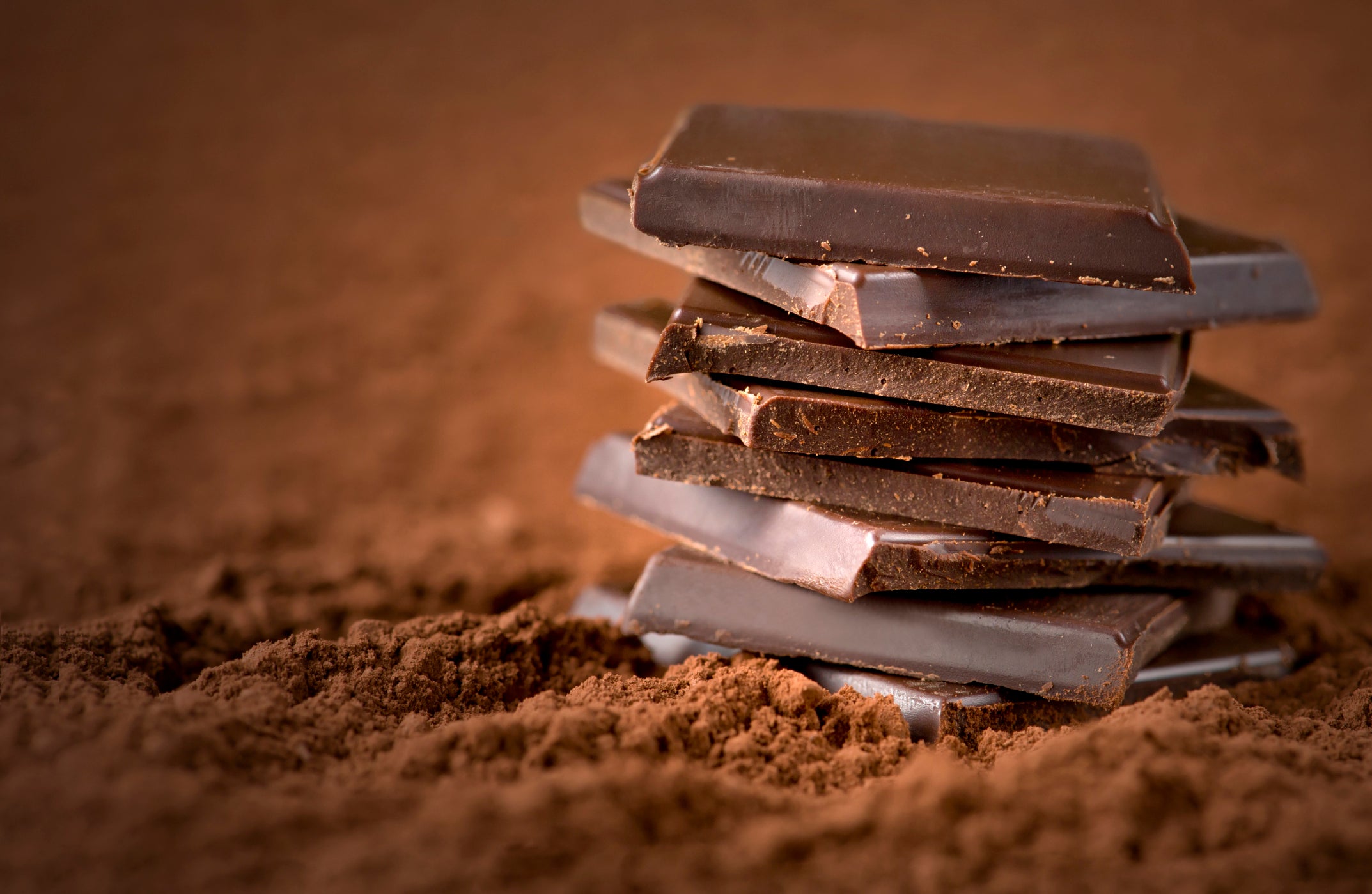 Stacked dark chocolate pieces resting on a textured surface of cocoa powder, highlighting the raw ingredients and expert market perspectives in cocoa commodities.