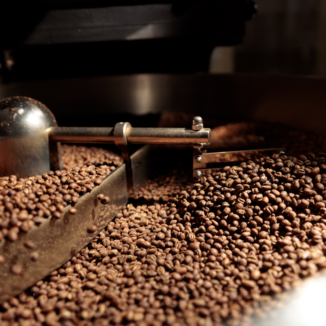 Close-up of freshly roasted coffee beans being stirred in a metal roasting drum, illustrating expert insights and exclusive market analysis for coffee commodity trends and report subscriptions.