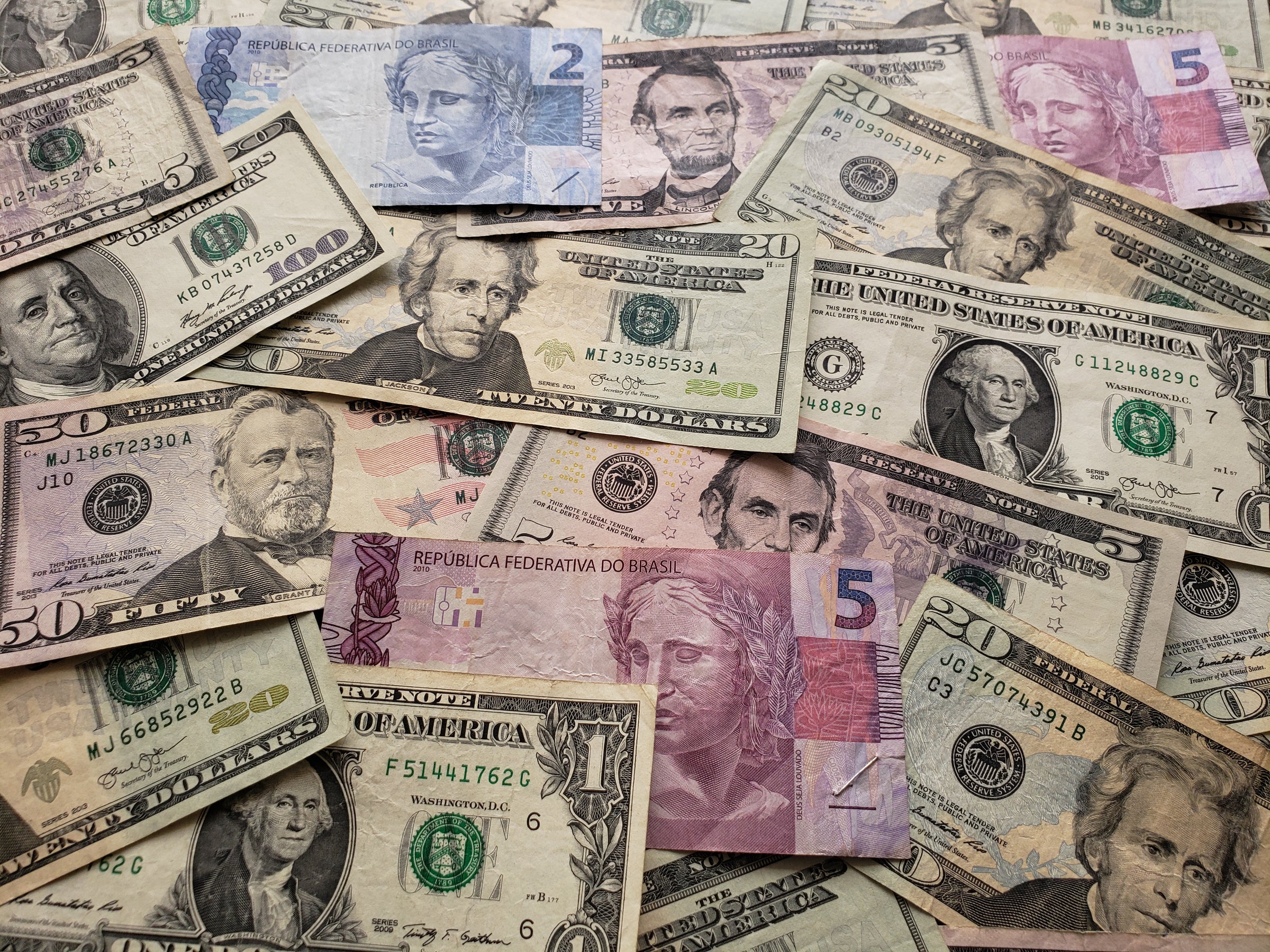 An assortment of US dollar and Brazilian real banknotes scattered on a surface, illustrating currency exchange and global market perspectives with expert analysis for market report subscriptions.