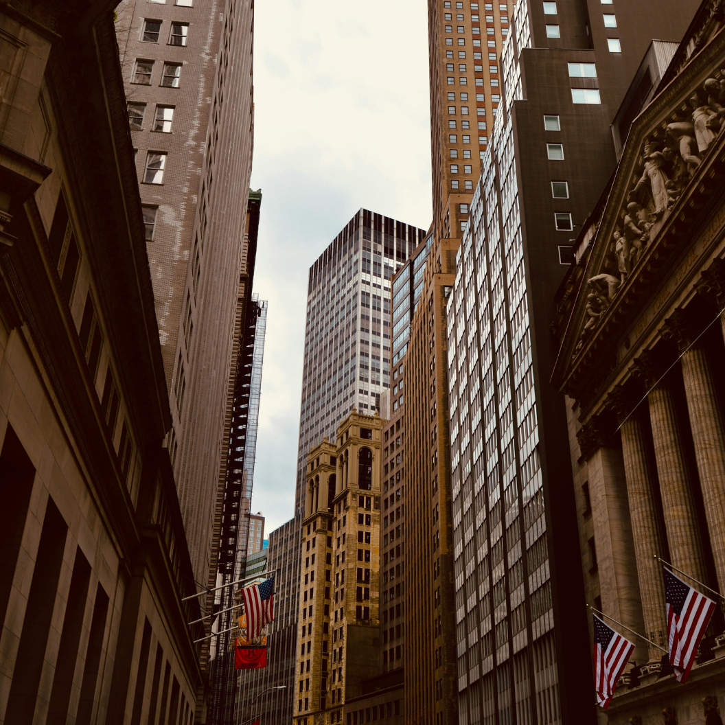 Urban canyon view of tall office buildings with American flags on historic facades, reflecting economic activity and market trends for expert insights and market report subscriptions.