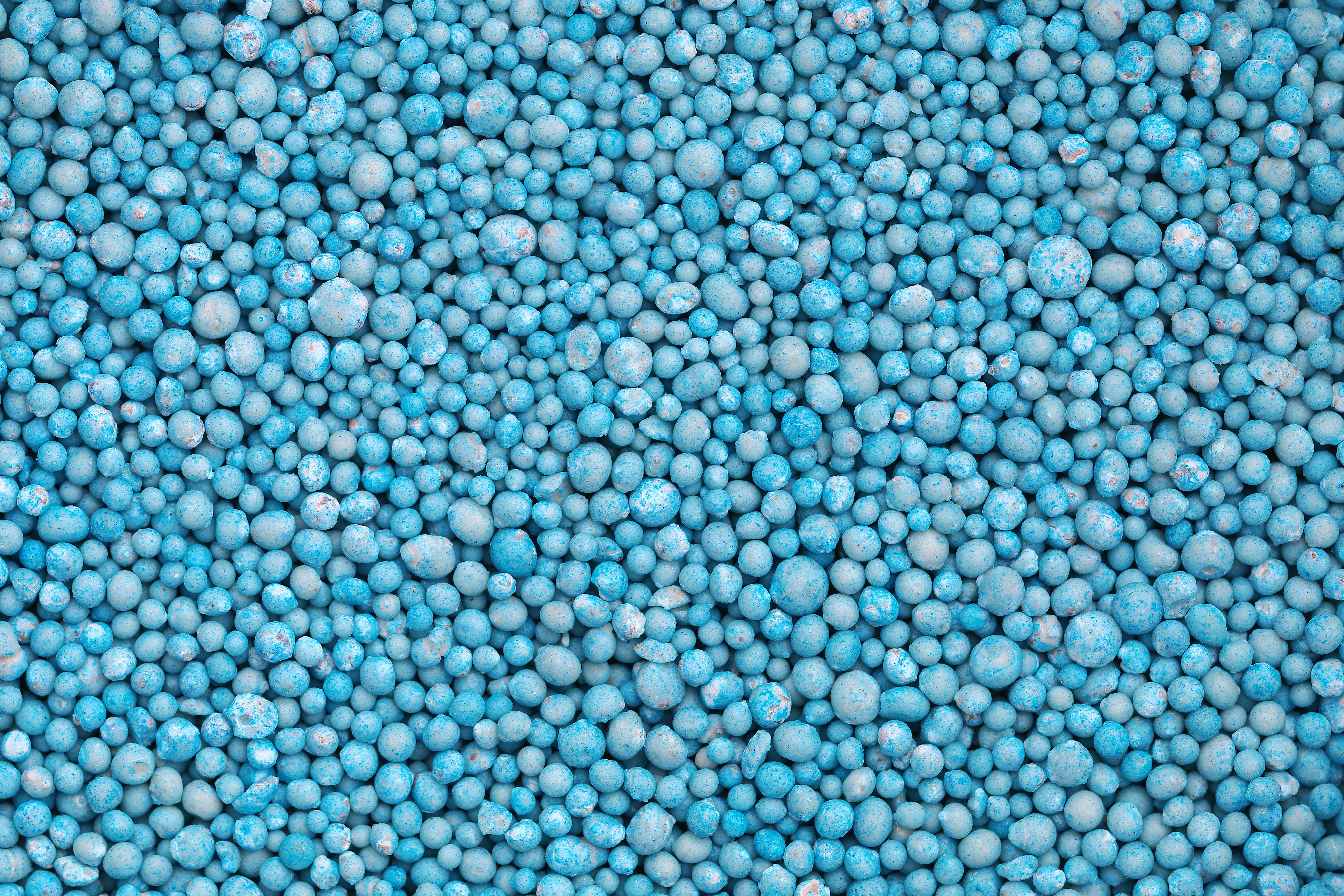 Close-up of numerous small blue fertilizer granules scattered densely, symbolizing agricultural commodity trends and expert market insights for report subscriptions.
