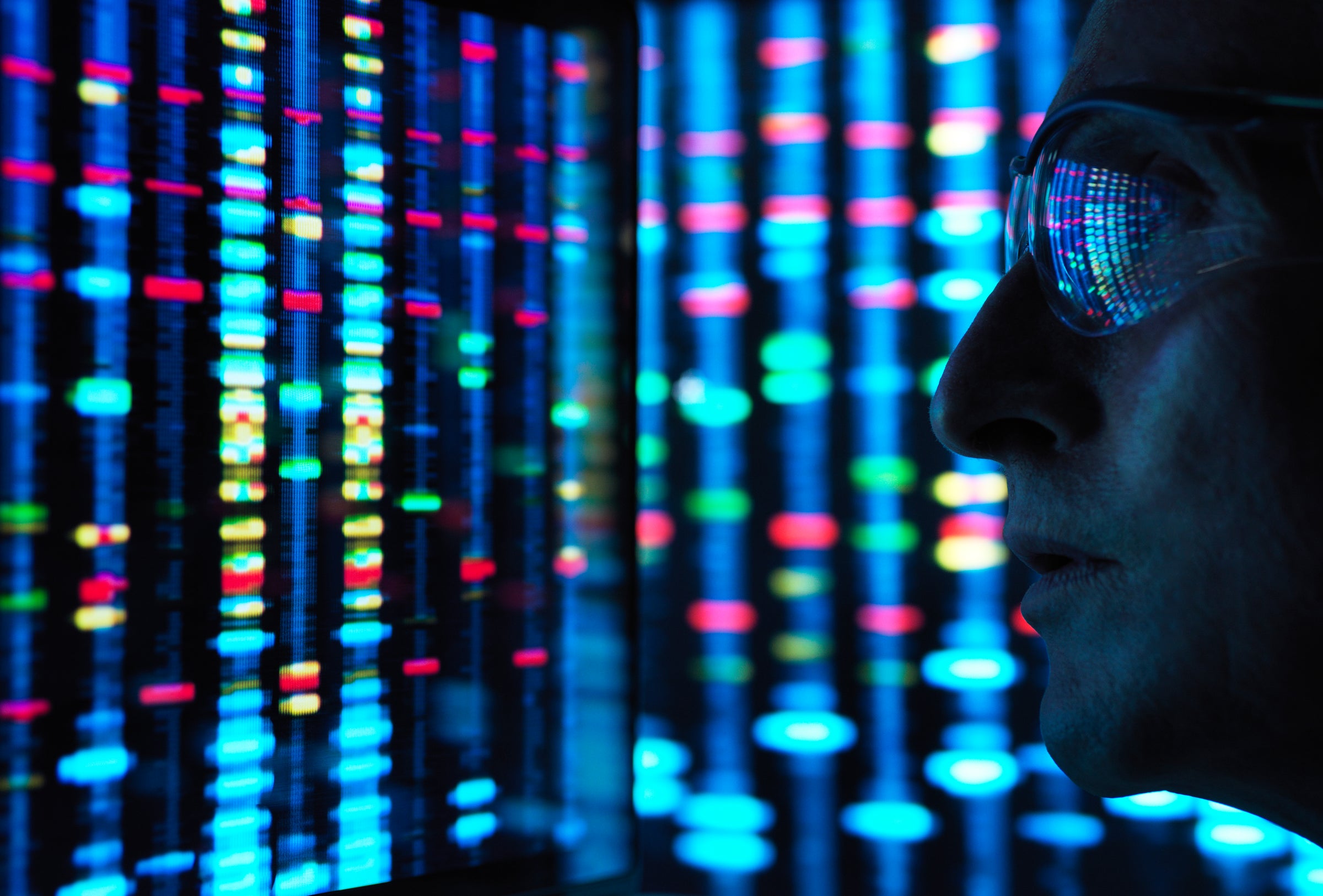 Close-up of an individual wearing glasses analyzing colorful digital data patterns on illuminated vertical screens, representing expert market intelligence and deep research insights.