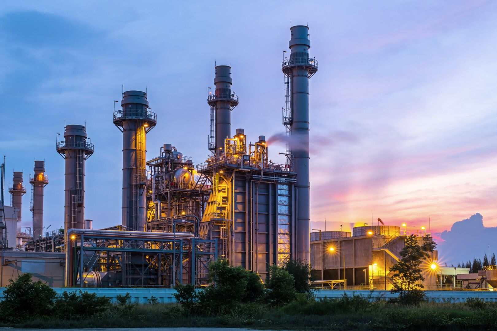 Industrial power plant with tall chimneys and complex piping structures illuminated against a dusk sky, illustrating energy sector trends and market intelligence analysis.