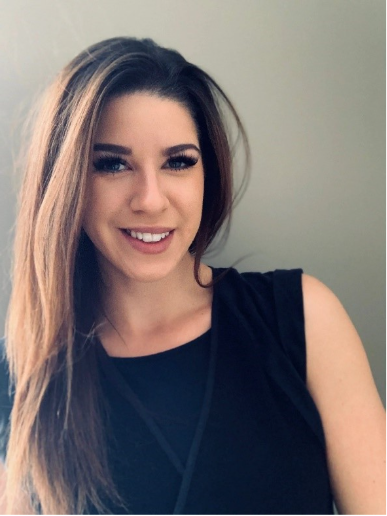 Young woman with long brown hair and natural makeup wearing a sleeveless black top, smiling warmly against a plain neutral background, conveying a professional and approachable presence.