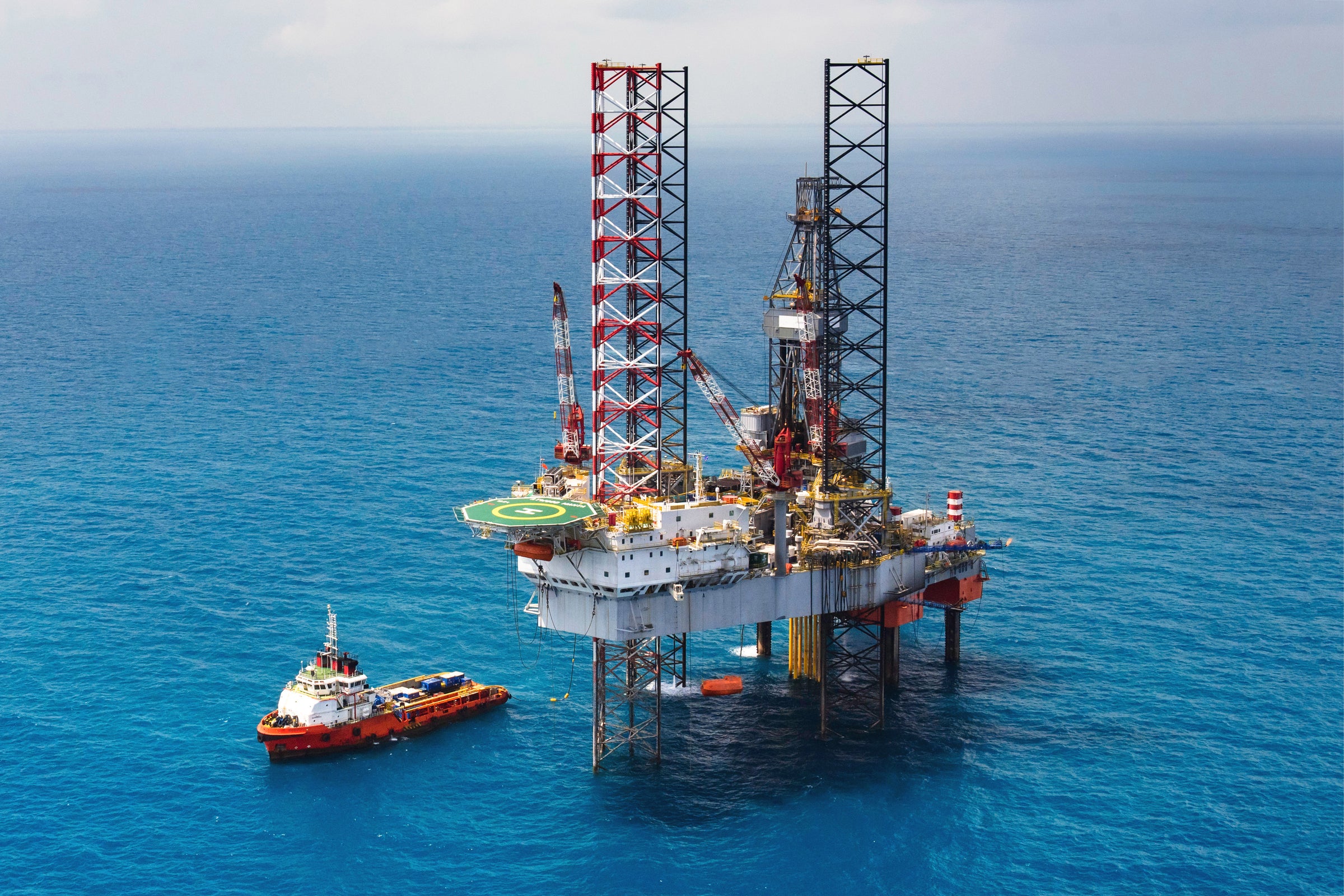 Offshore drilling rig positioned in calm blue ocean waters with a supply vessel nearby, illustrating energy commodity trends and expert insights for market reports and outlook perspectives.