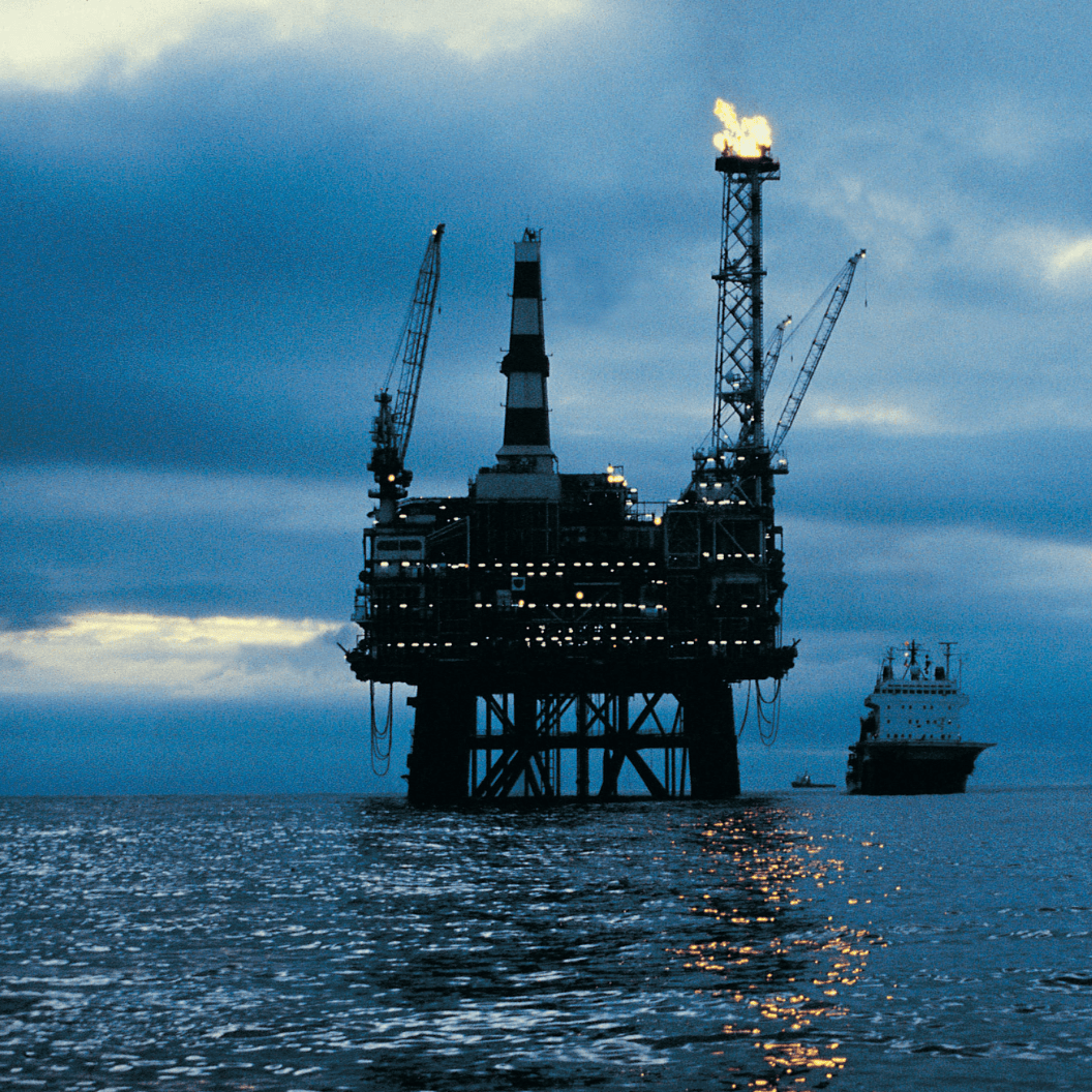 Offshore oil platform stands illuminated at dusk with cranes and gas flare, a supply vessel nearby on calm waters, reflecting expert insights and exclusive market analysis.