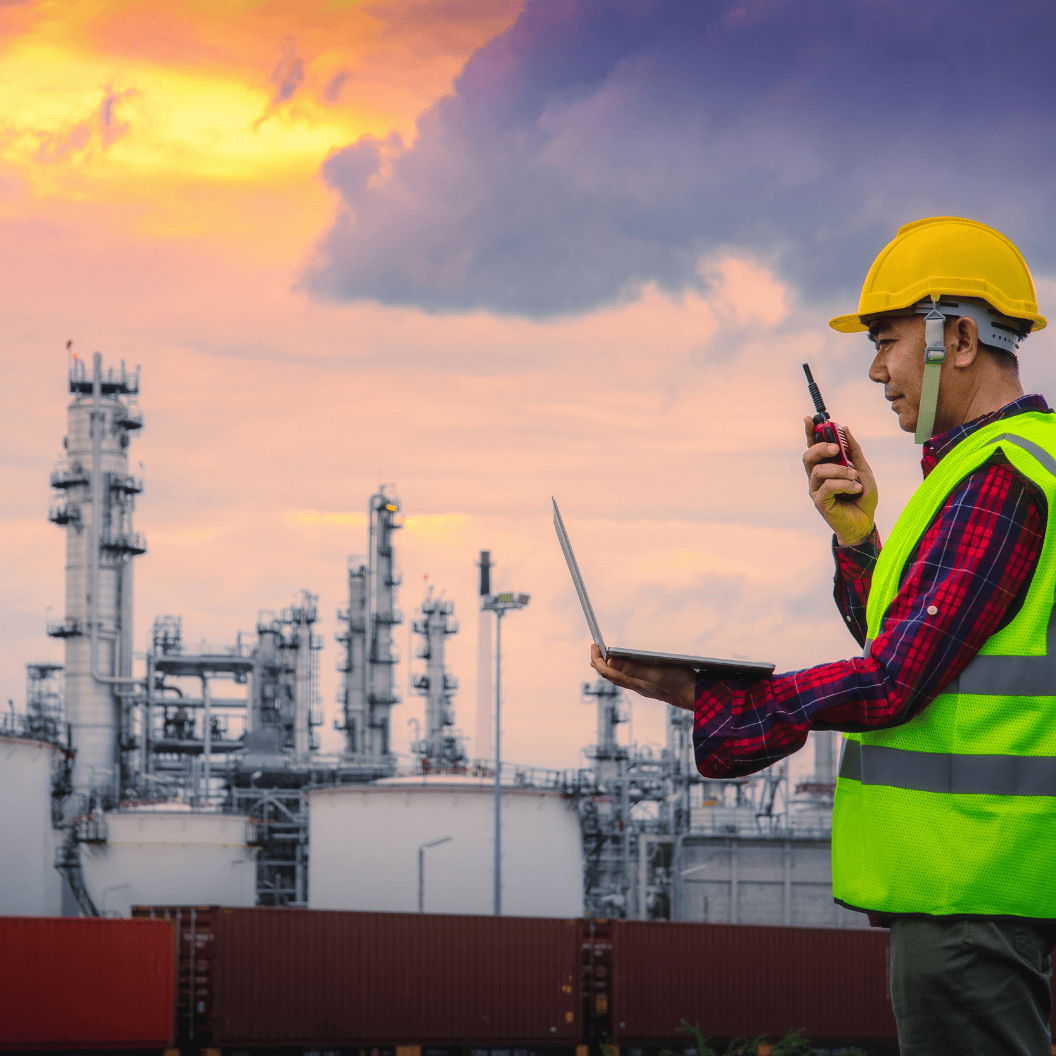 Engineer wearing safety gear uses a walkie-talkie and laptop while inspecting an industrial oil refinery at sunset, illustrating expert insights and exclusive market analysis for energy commodity trends and Market Reports Subscriptions.