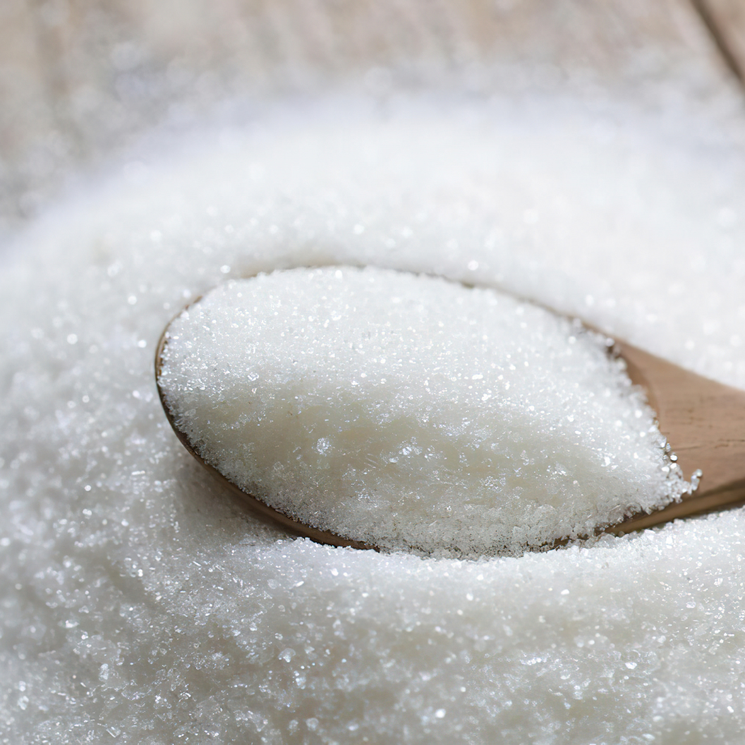 Close-up of granulated white sugar crystals heaped in a wooden spoon against a background of loose sugar, illustrating expert insights and exclusive market analysis for sugar commodity trends and report subscriptions.