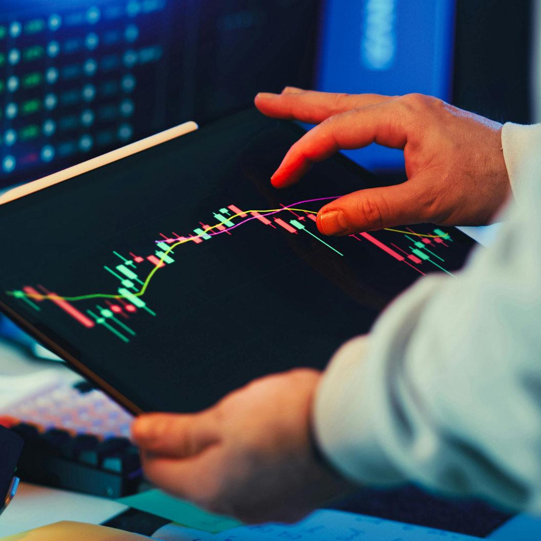 Close-up of a person analyzing colorful candlestick charts on a digital tablet, representing tactical market strategies and expert insights in market reports subscriptions and commodity trends.